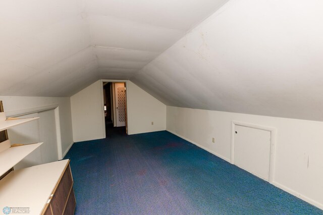additional living space with vaulted ceiling, baseboards, and dark carpet