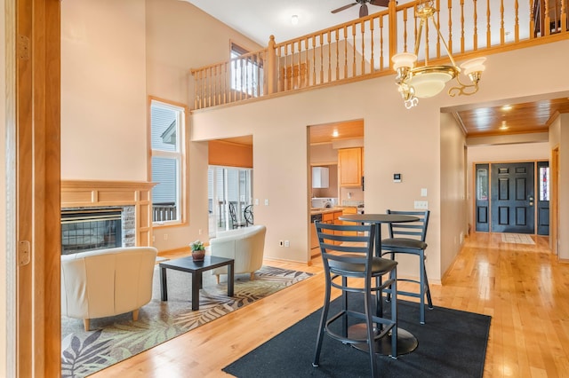 dining area with wood finished floors, a towering ceiling, a fireplace, and ceiling fan with notable chandelier