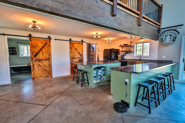 kitchen with open shelves, a kitchen breakfast bar, a barn door, black appliances, and green cabinets