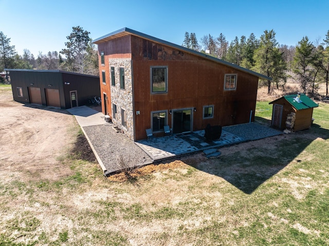 back of property featuring a garage, an outbuilding, a yard, and a patio