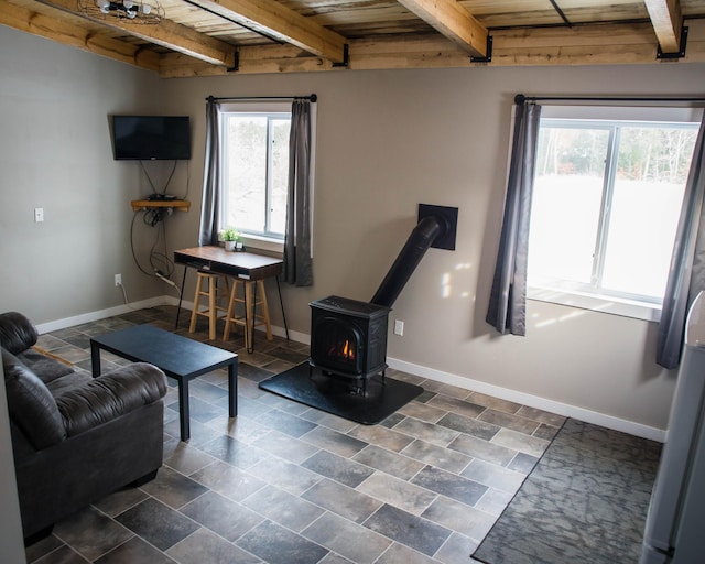 living area with beamed ceiling, wooden ceiling, baseboards, and a wood stove