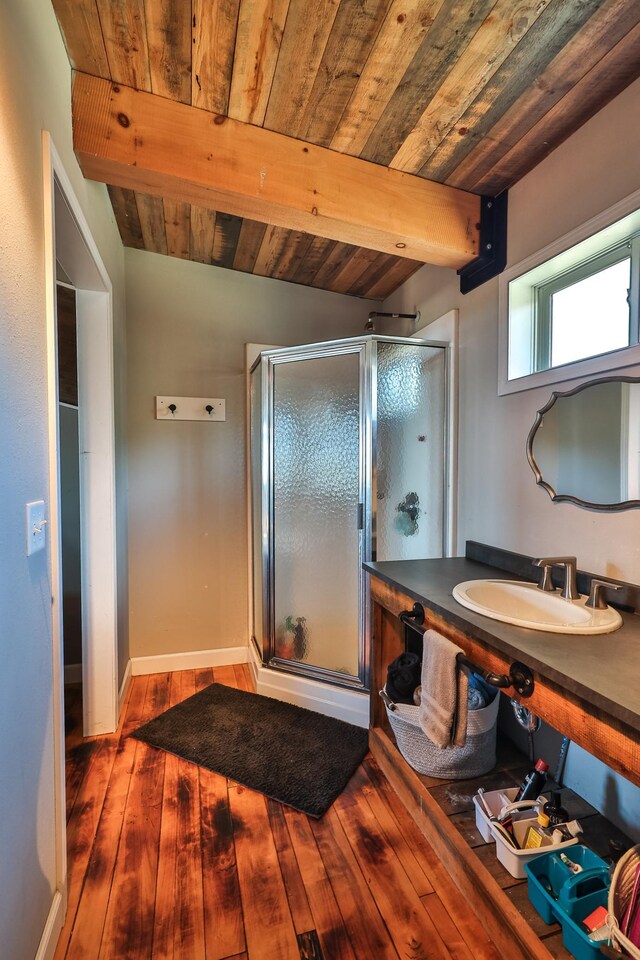 bathroom featuring a shower stall, beam ceiling, wood finished floors, a sink, and wooden ceiling