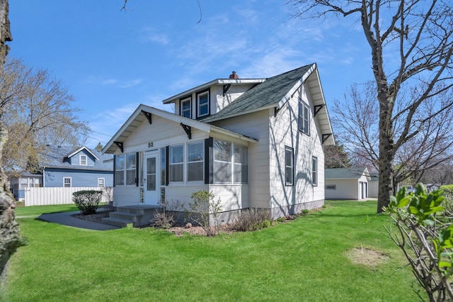 view of side of home with a lawn, fence, a chimney, and a shingled roof