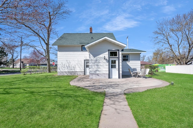 rear view of house with fence, a patio, roof with shingles, a chimney, and a yard