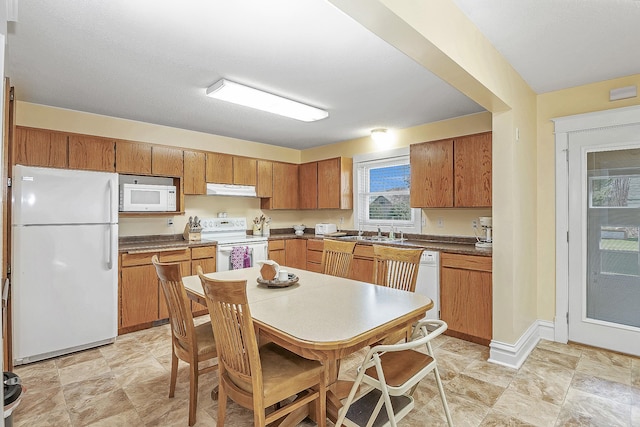 kitchen with dark countertops, a sink, white appliances, brown cabinetry, and under cabinet range hood