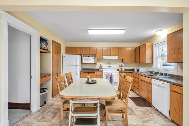 kitchen featuring brown cabinets, dark countertops, a sink, white appliances, and under cabinet range hood