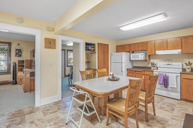 kitchen featuring brown cabinetry, dark countertops, white appliances, baseboards, and under cabinet range hood