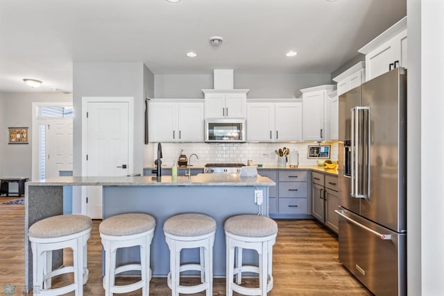 kitchen featuring a kitchen breakfast bar, wood finished floors, decorative backsplash, white cabinets, and appliances with stainless steel finishes