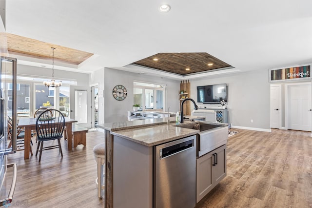 kitchen featuring a raised ceiling, stainless steel dishwasher, a sink, a center island with sink, and open floor plan