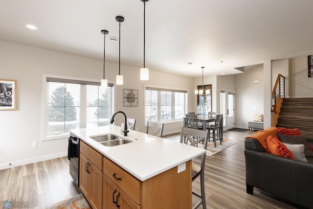 kitchen featuring light wood-type flooring, a sink, light countertops, open floor plan, and an island with sink