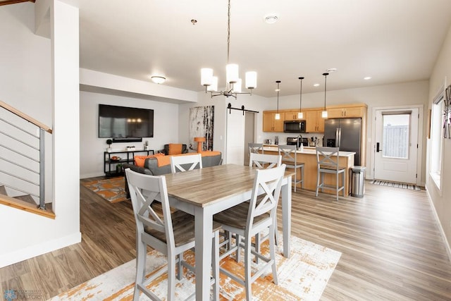 dining room featuring a notable chandelier, a barn door, light wood-style floors, baseboards, and stairway