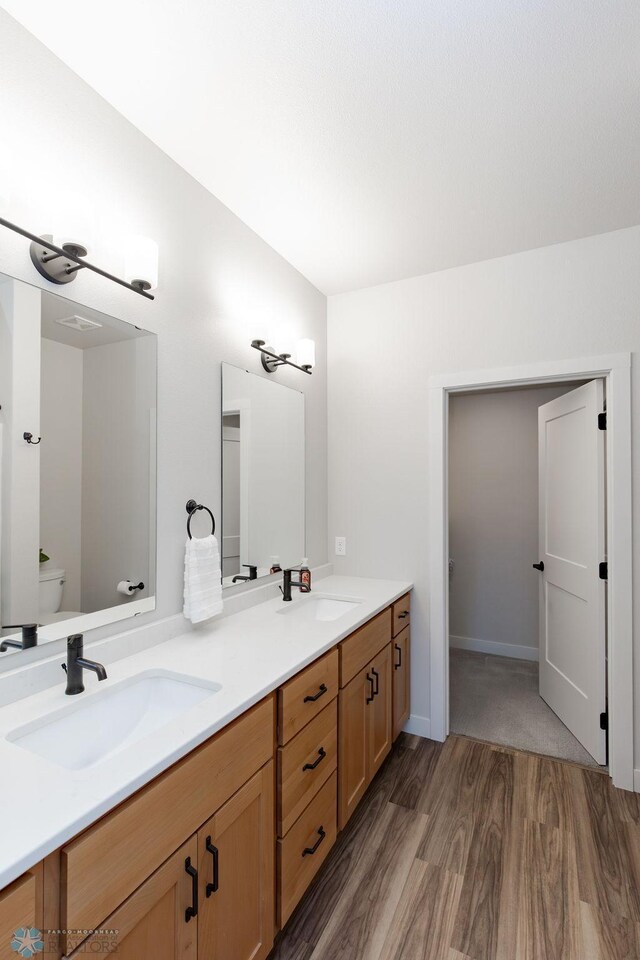 full bathroom with a sink, toilet, double vanity, and wood finished floors