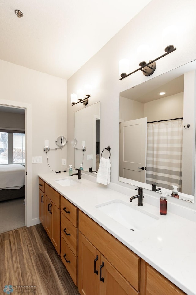ensuite bathroom featuring double vanity, a sink, ensuite bath, and wood finished floors