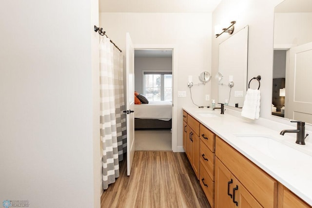 full bath with a sink, double vanity, wood finished floors, and connected bathroom