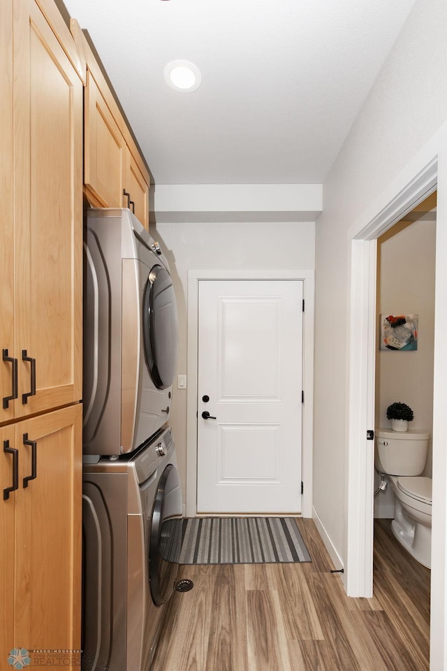 clothes washing area featuring baseboards, cabinet space, stacked washing maching and dryer, and wood finished floors
