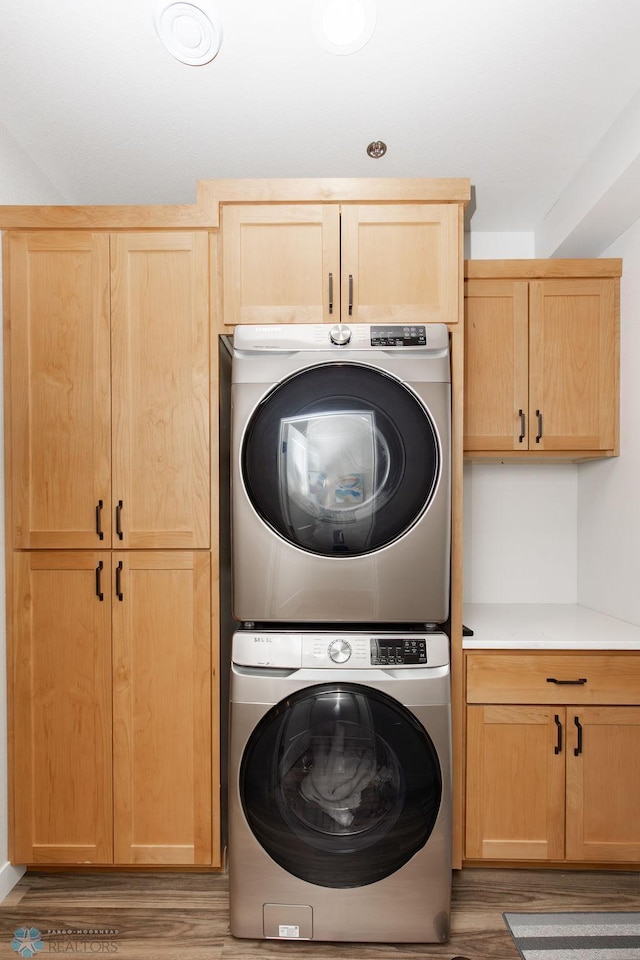 laundry area featuring light wood-type flooring, cabinet space, and stacked washer / dryer