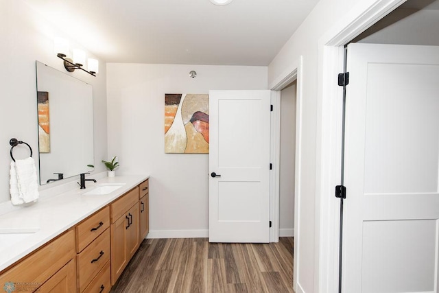 full bathroom with a sink, baseboards, double vanity, and wood finished floors