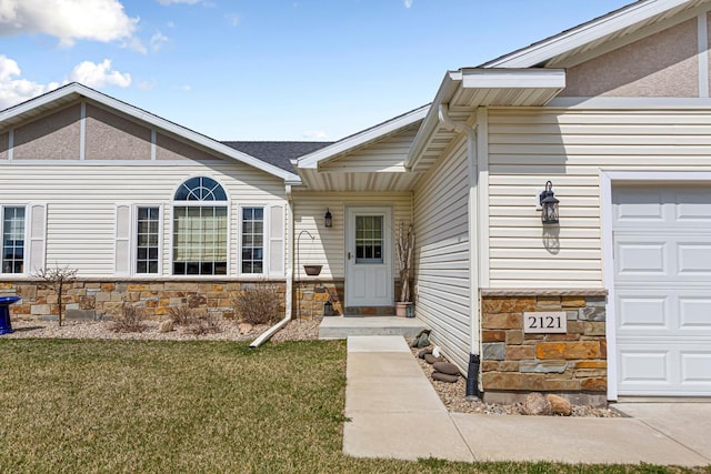 doorway to property with an attached garage, a lawn, and stone siding