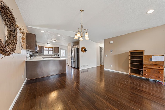 unfurnished living room featuring dark wood-style floors, baseboards, visible vents, a notable chandelier, and lofted ceiling