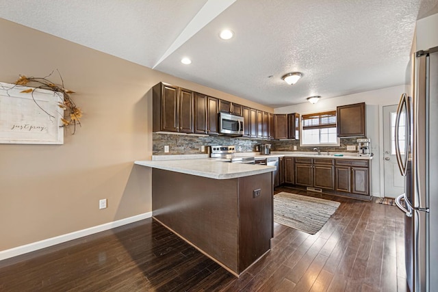 kitchen featuring light countertops, dark brown cabinets, baseboards, a peninsula, and appliances with stainless steel finishes