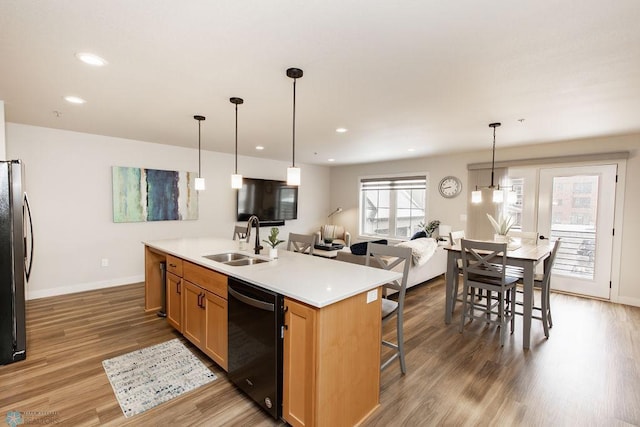kitchen featuring a kitchen island with sink, wood finished floors, a sink, black appliances, and recessed lighting
