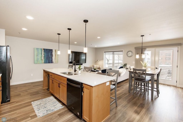 kitchen featuring wood finished floors, open floor plan, an island with sink, a sink, and black appliances
