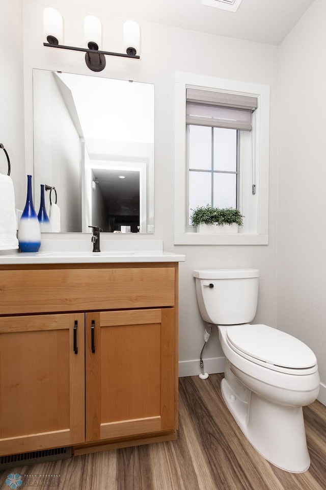half bathroom with baseboards, wood finished floors, toilet, and vanity