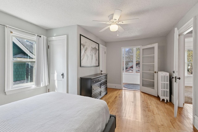 bedroom with french doors, a textured ceiling, light wood-type flooring, baseboards, and radiator heating unit