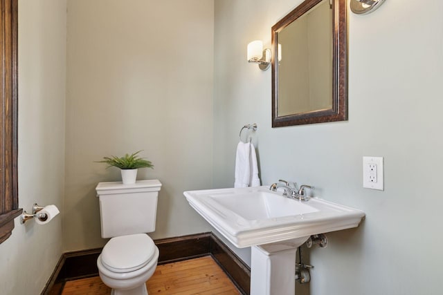 half bath with baseboards, wood-type flooring, and toilet