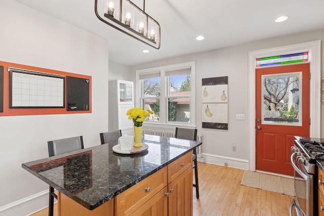 kitchen with a breakfast bar, stainless steel gas range oven, light wood-style floors, dark stone counters, and recessed lighting