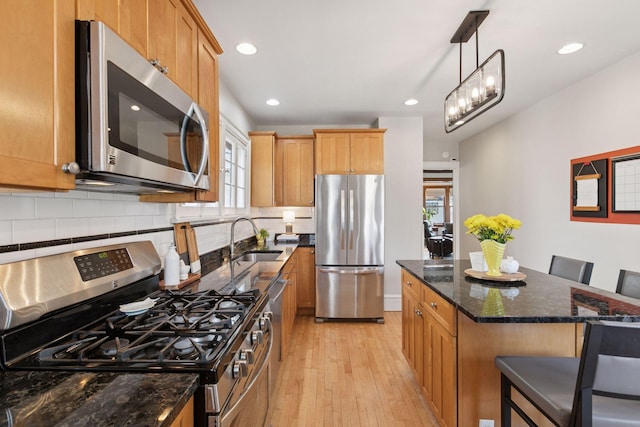kitchen with decorative backsplash, appliances with stainless steel finishes, a sink, dark stone countertops, and light wood-style flooring