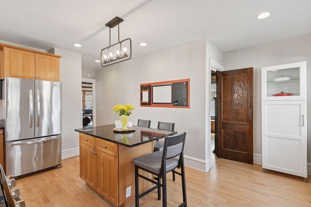 kitchen with freestanding refrigerator, a breakfast bar, light wood finished floors, and a center island