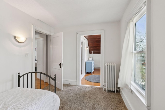 carpeted bedroom with baseboards, radiator heating unit, and ensuite bath
