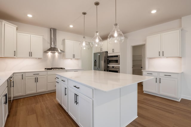 kitchen with stainless steel appliances, wall chimney range hood, wood finished floors, a kitchen island, and recessed lighting