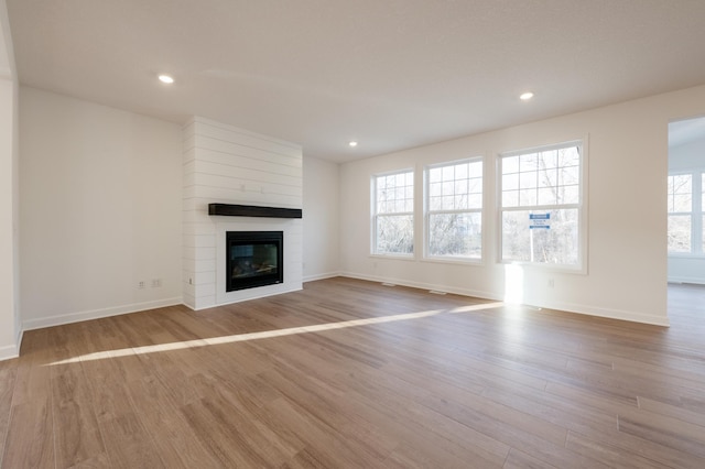 unfurnished living room with wood finished floors, a fireplace, baseboards, and recessed lighting