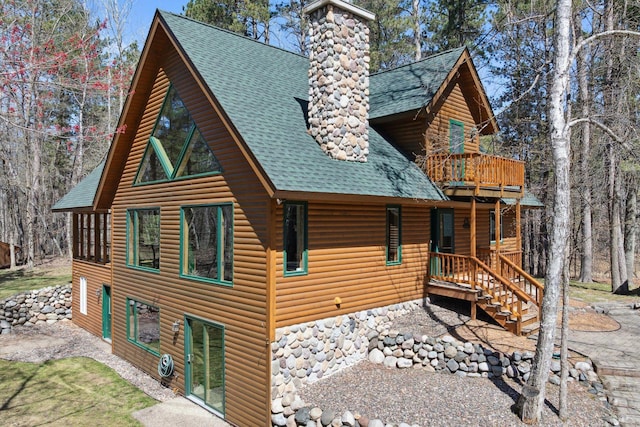 view of side of home with roof with shingles, a chimney, faux log siding, and a balcony