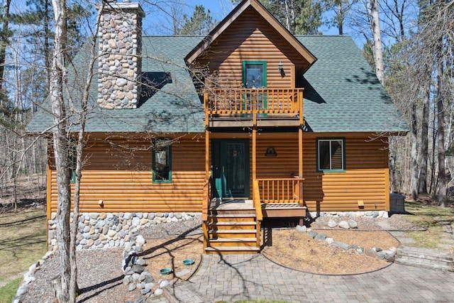 chalet / cabin featuring a shingled roof, a balcony, and a chimney