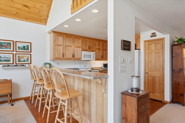 kitchen featuring white appliances, a kitchen breakfast bar, recessed lighting, baseboards, and a peninsula
