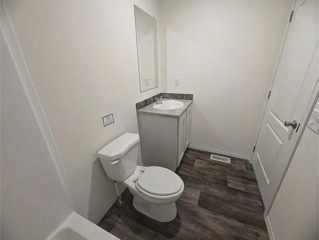 bathroom with vanity, toilet, visible vents, baseboards, and wood finished floors