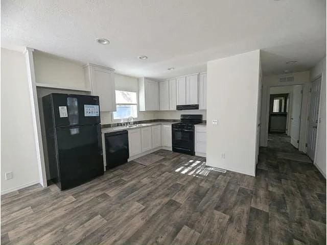 kitchen with white cabinets, a sink, dark wood-style floors, under cabinet range hood, and black appliances