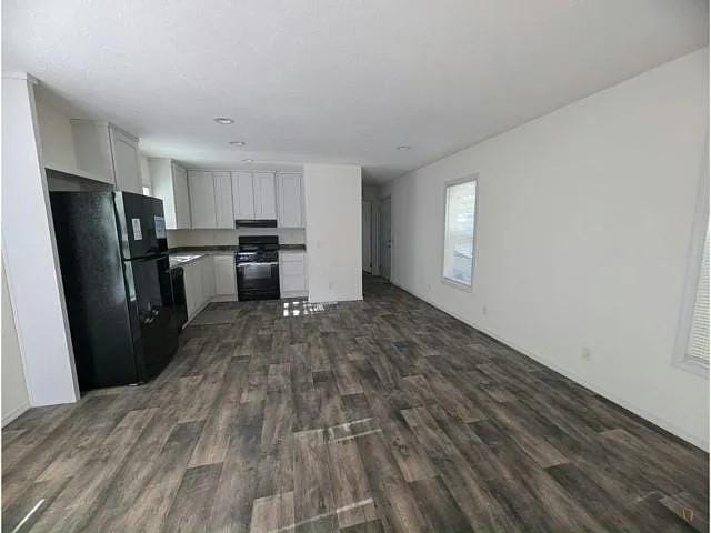 kitchen featuring white cabinetry, dark wood-style floors, under cabinet range hood, black appliances, and open floor plan