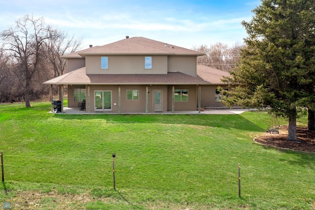 rear view of house featuring a patio, a lawn, and roof with shingles