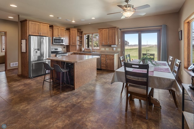 kitchen with visible vents, appliances with stainless steel finishes, a center island, brown cabinets, and a sink