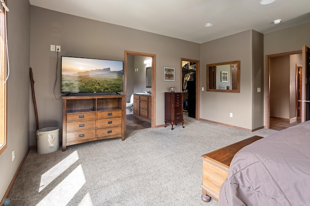 bedroom featuring a walk in closet, light colored carpet, baseboards, a closet, and ensuite bathroom