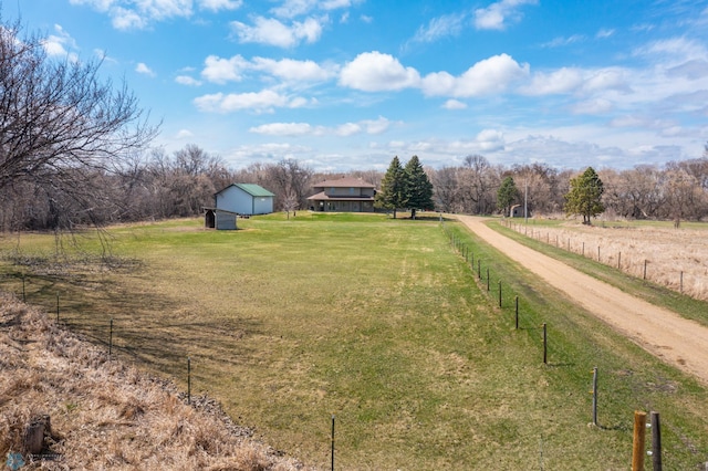 view of yard with an outdoor structure, fence, driveway, and a rural view
