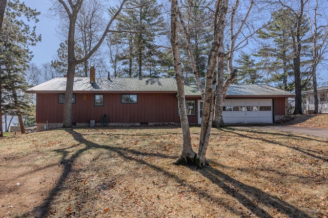 view of front of home featuring a chimney, metal roof, an attached garage, and driveway