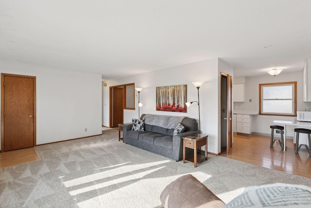 living area with baseboards, light wood-style flooring, and light colored carpet