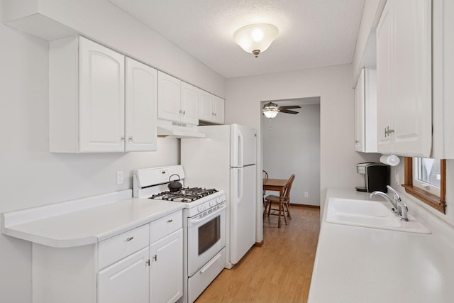 kitchen with a ceiling fan, a sink, light wood finished floors, white appliances, and white cabinetry