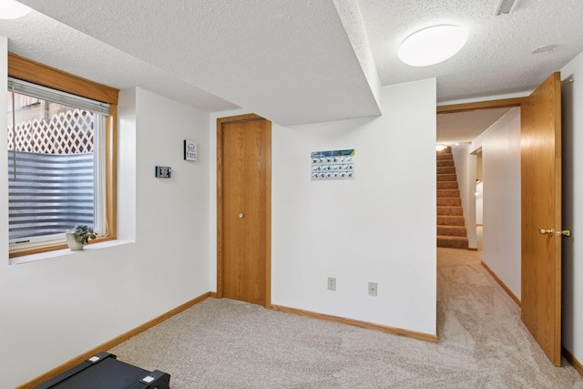spare room with a textured ceiling, visible vents, light colored carpet, stairway, and baseboards