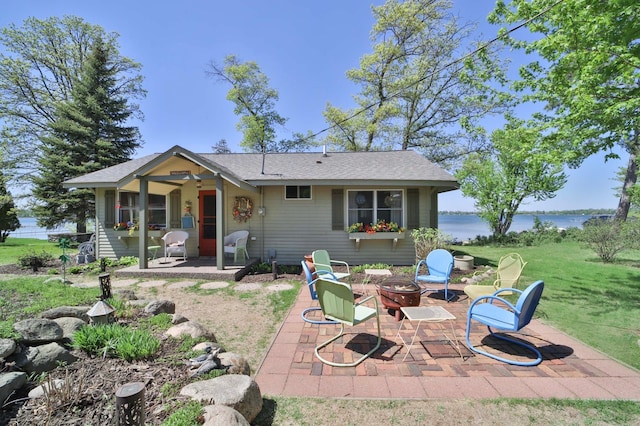 rear view of house with an outdoor fire pit, a patio area, a water view, a lawn, and a shingled roof